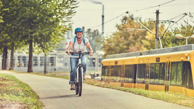 Eine Frau fährt ein Fahrrad. Neben dem Radweg fährt eine Straßenbahn.