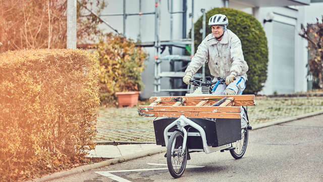 Eine Frau fährt auf einem Lastenrad und transportiert damit eine Leiter.